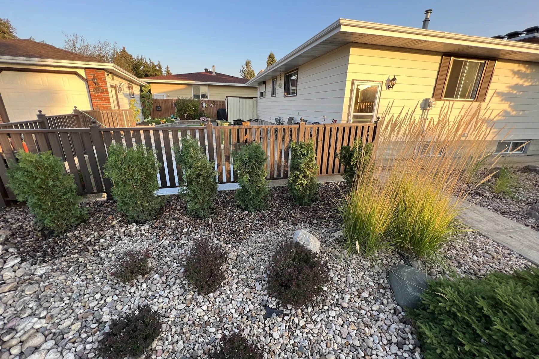 River rock xeriscape garden with juniper shrubs and ornamental grass, Calgary softscape design by All The Moore