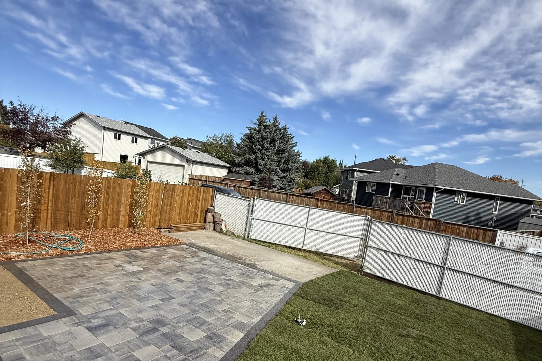 Completed Calgary backyard with large interlocking paver patio, fresh sod, and cedar fence by All The Moore Landscaping