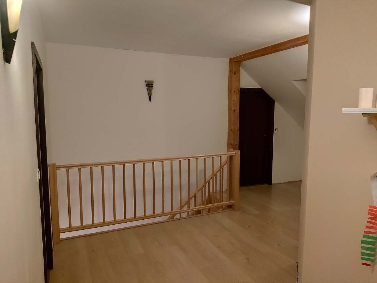Chodba v patře s dřevěným zábradlím nad schodištěm, světlou podlahou a průchodem se zkoseným stropem