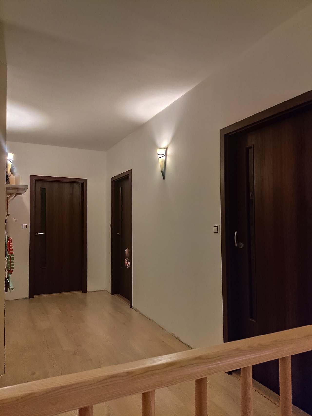 Chodba v patře s dřevěnými dveřmi do pokojů, světlou podlahou a nástěnnými svítidly