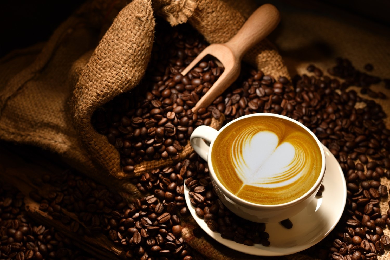 Warm latte art with a heart pattern surrounded by coffee beans and a burlap sack
