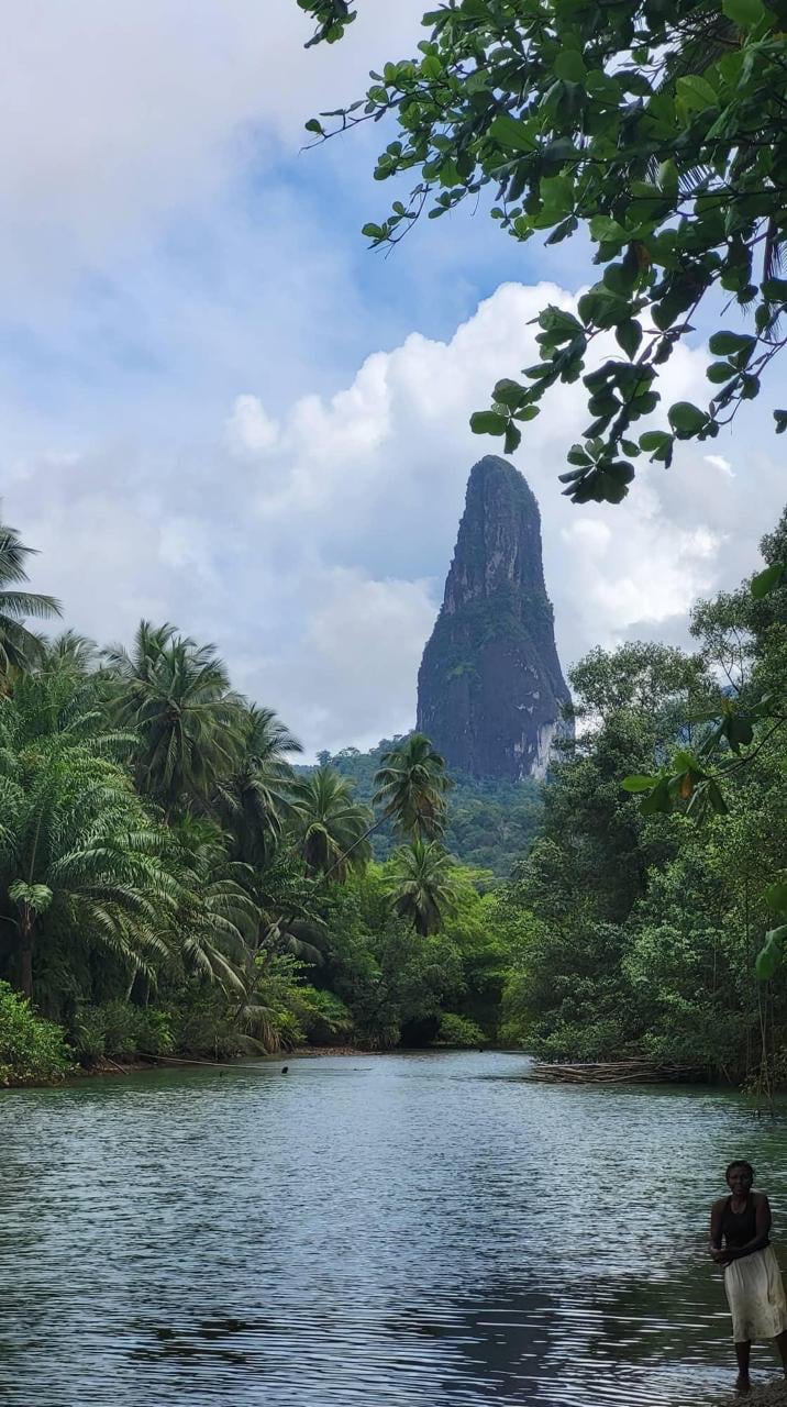 Uma pessoa a vadear numa lagoa com o Pico Cão Grande a erguer-se acima da floresta tropical em fundo