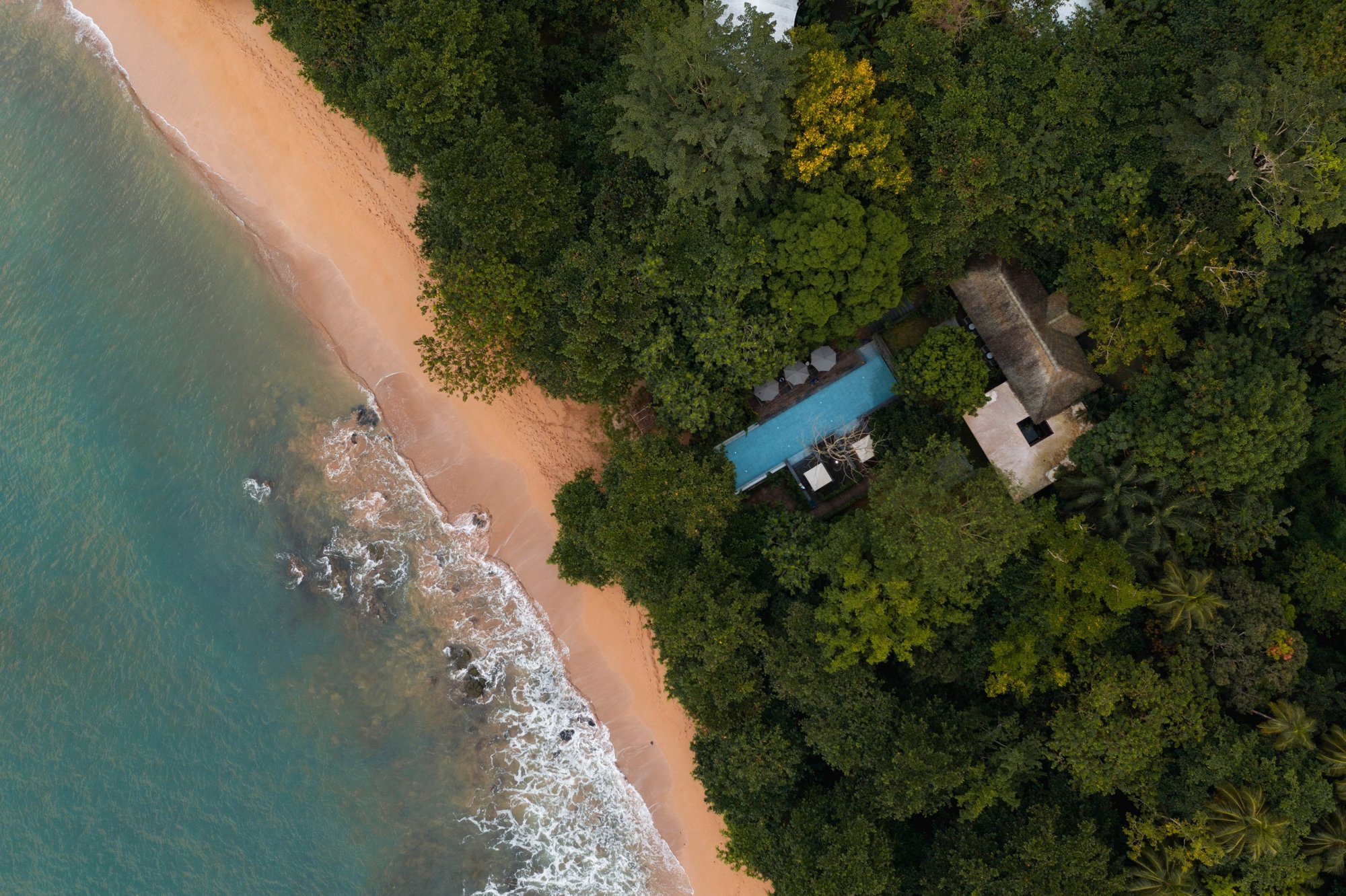 Overhead view of the pool deck and beach at Sundy Praia with loungers shaded by tropical trees