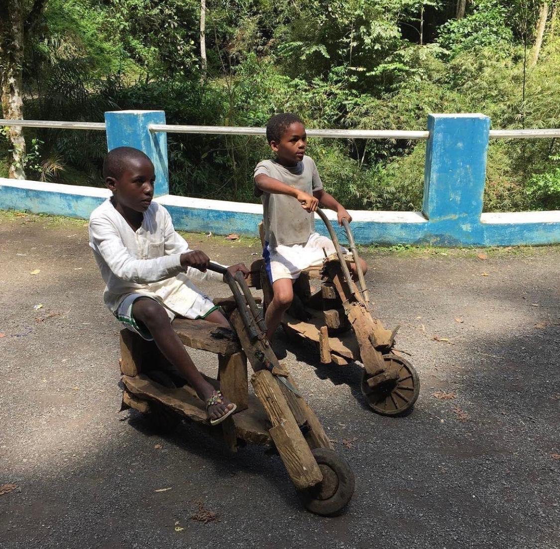 Boys riding handmade wooden bikes along a road in central São Tomé