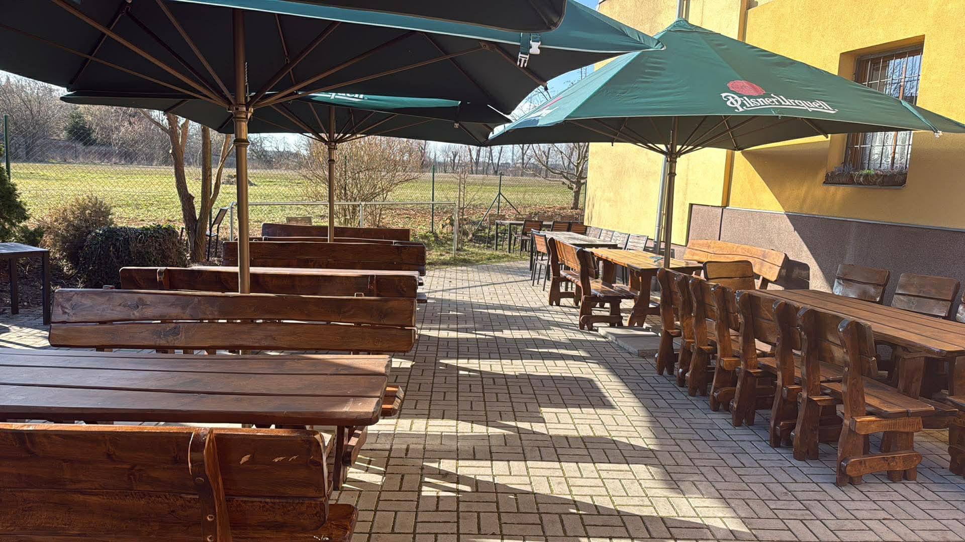 Letní terasa hostince Pod Vrbou s dřevěnými stoly a slunečníky Pilsner Urquell