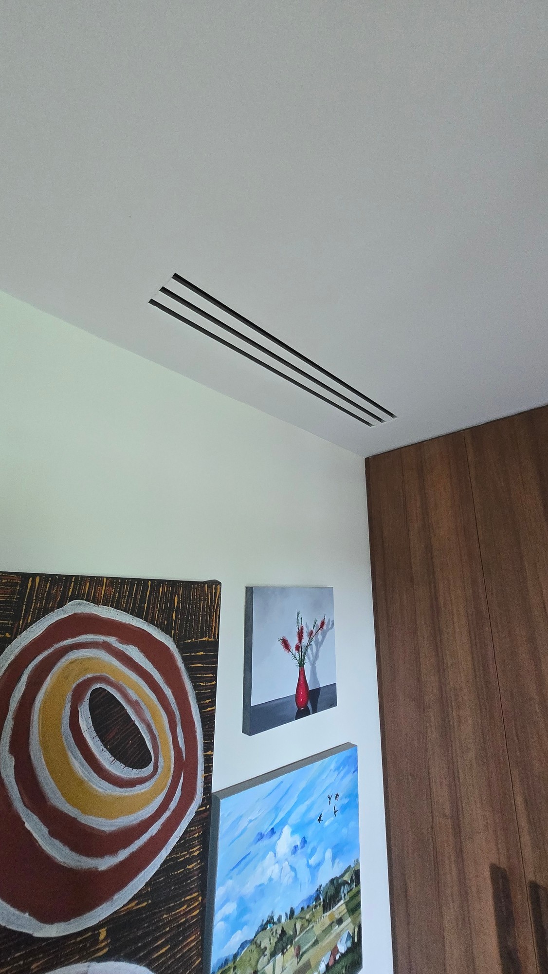 Minimal black slot grilles in white ceiling above an art-filled gallery wall