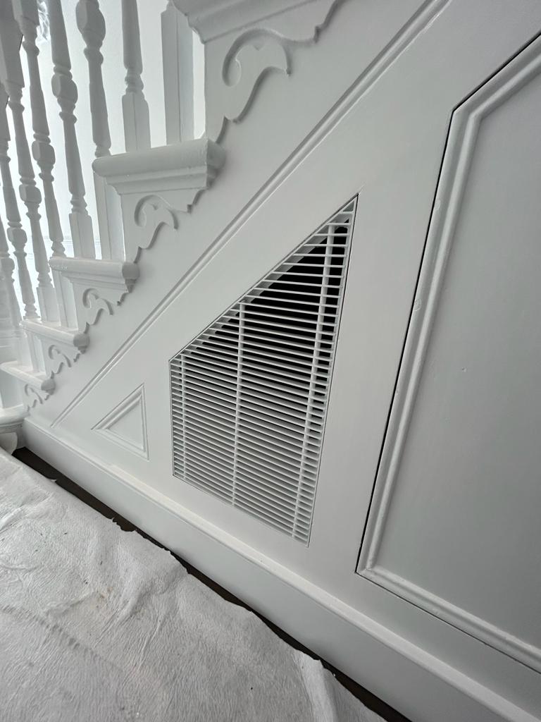 Custom triangular architectural grille integrated into heritage white staircase panel