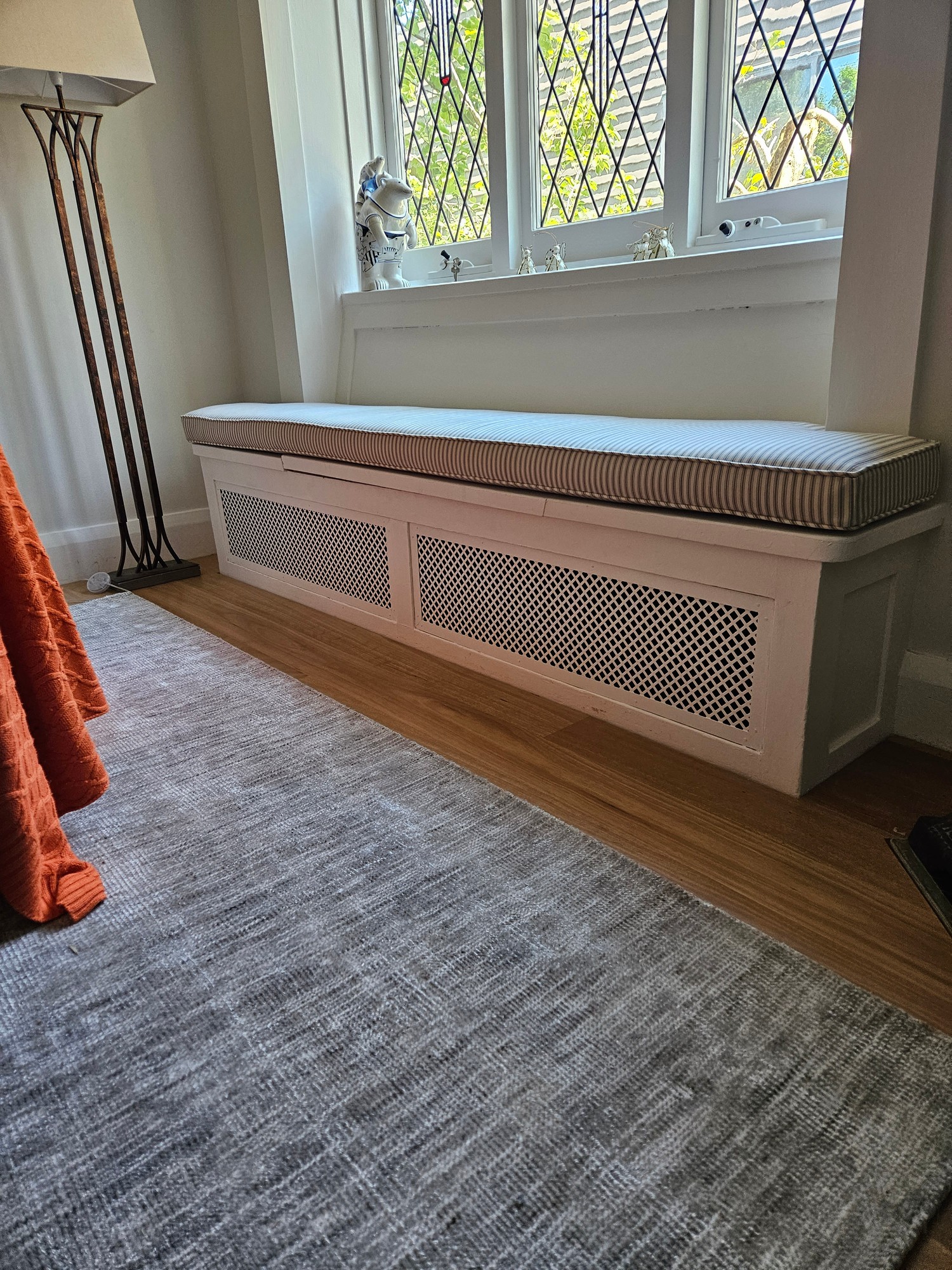 Mesh grille panel concealed within a white upholstered window seat bench