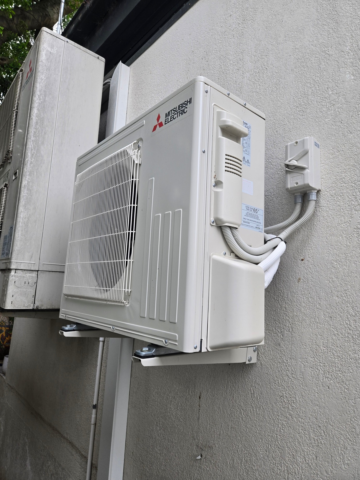 Mitsubishi Electric outdoor condenser unit wall-mounted on rendered external wall