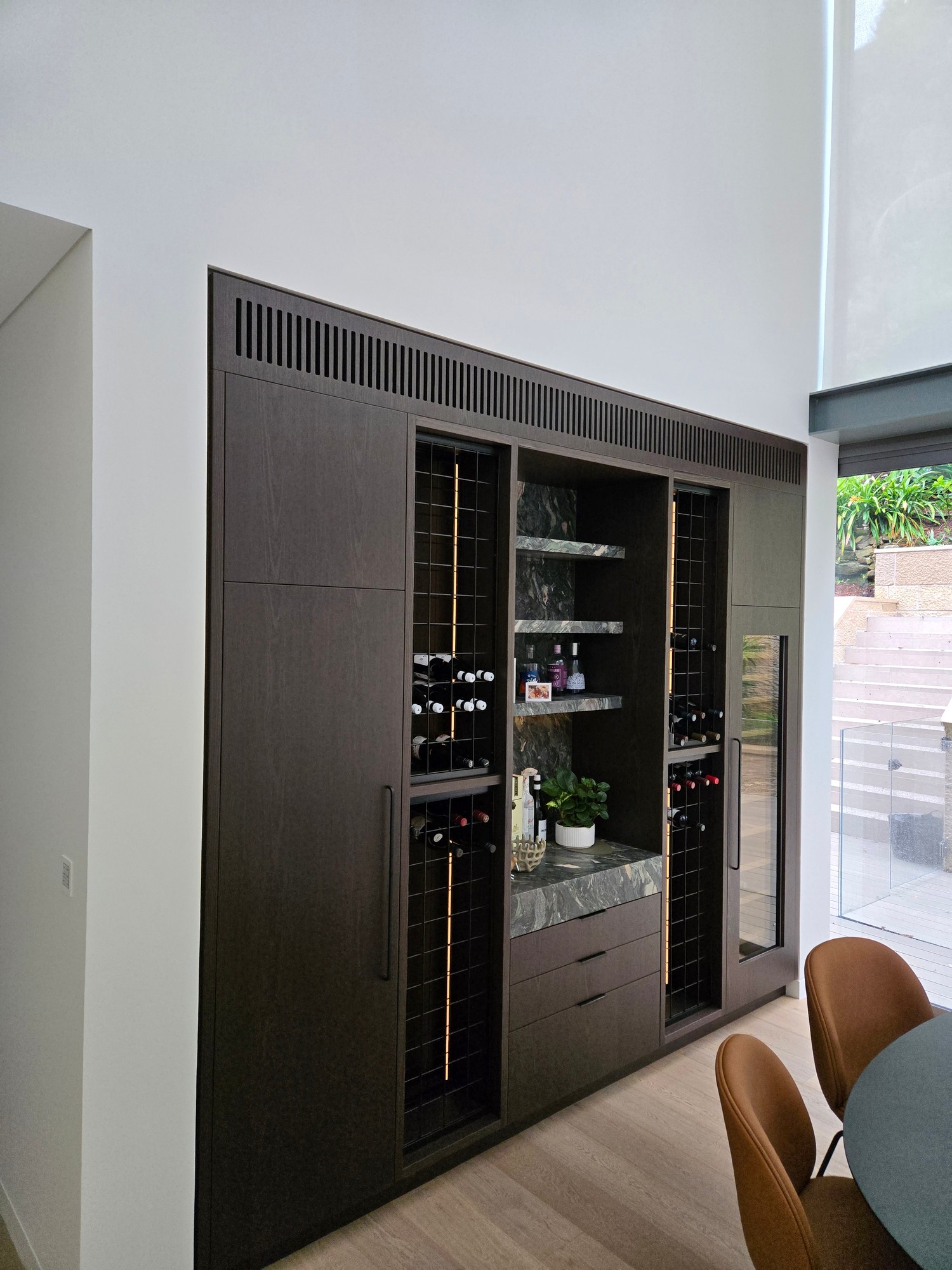 Slatted grilles integrated into dark timber wine cabinet and bar joinery