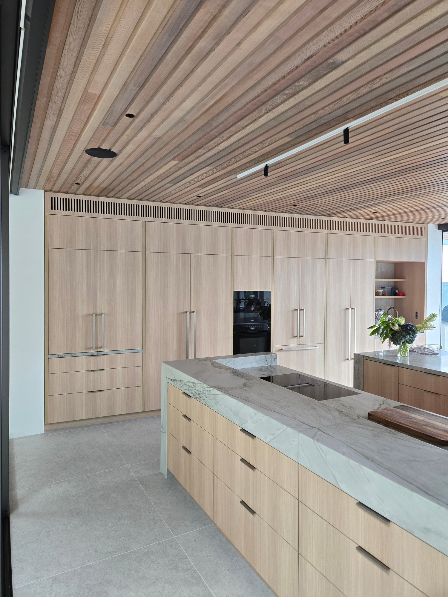 Linear grille integrated into light timber kitchen cabinetry wall panel