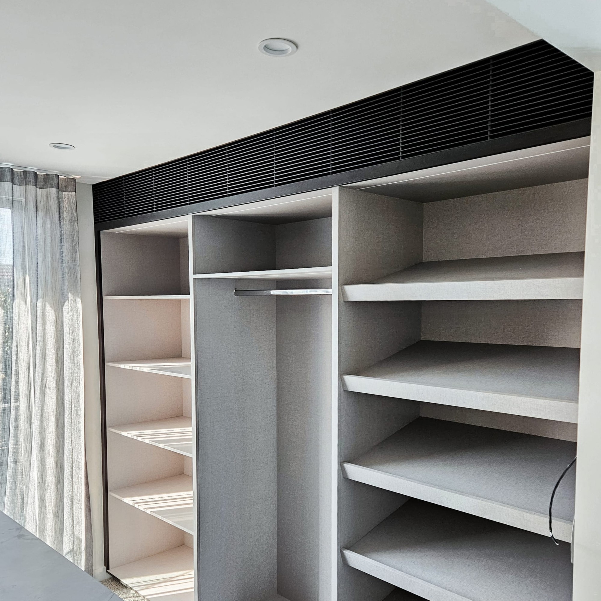 Dark linear grille concealed above bespoke wardrobe and shelving unit