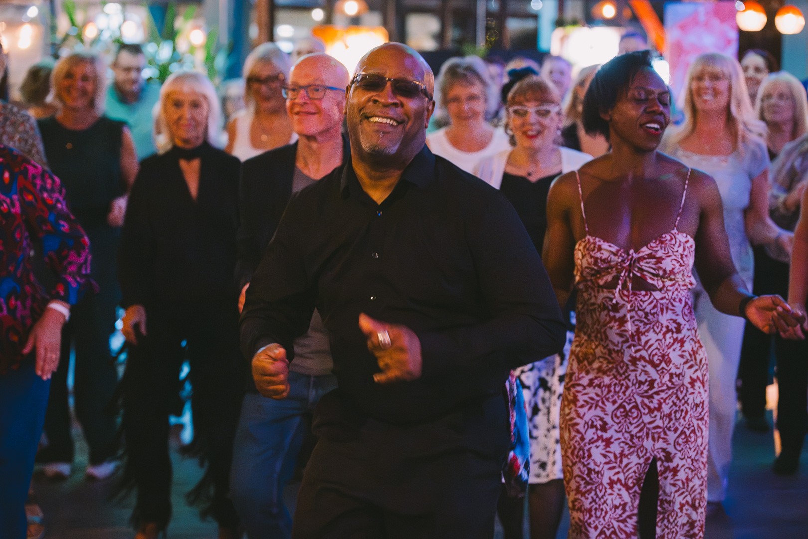 A lively Latin dance social evening with smiling dancers under warm string lights