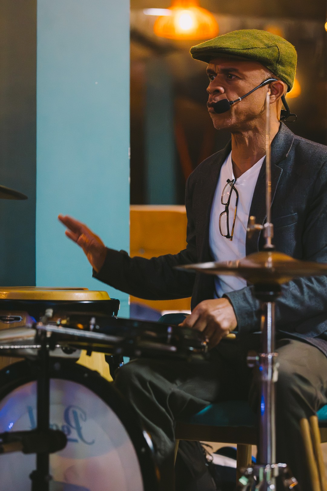 A musician in a flat cap with a headset microphone playing congas at the social night
