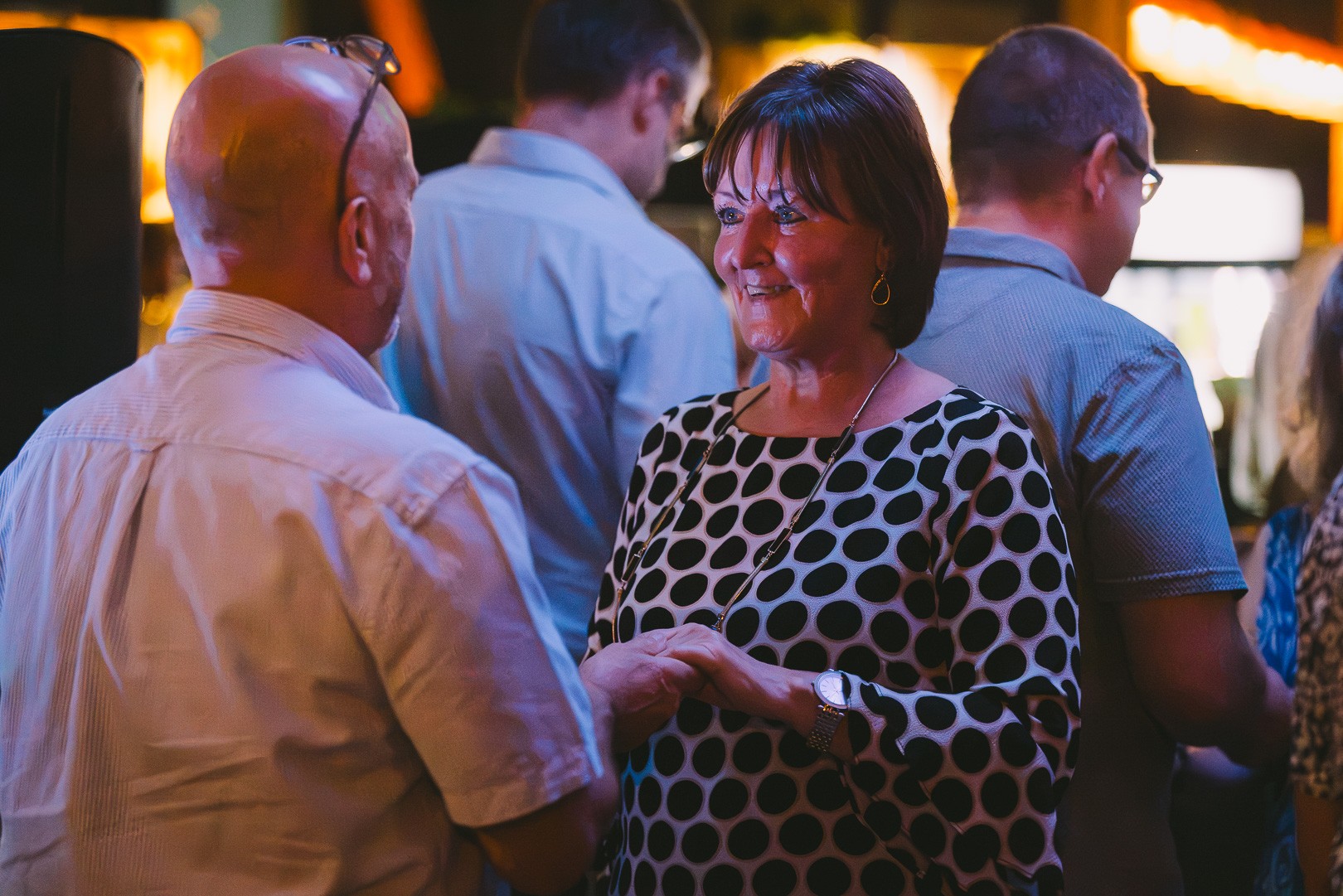A woman in a polka-dot dress smiling as she dances in the crowd at a social night