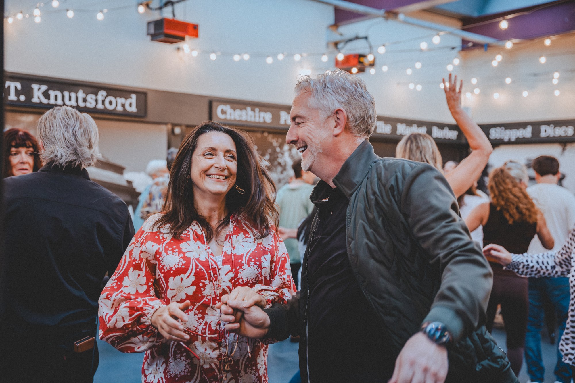 Dancers enjoying a salsa social night, a smiling couple holding hands under the string lights