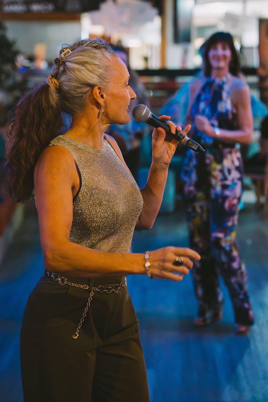 A woman singing into a microphone while dancers enjoy the party behind her