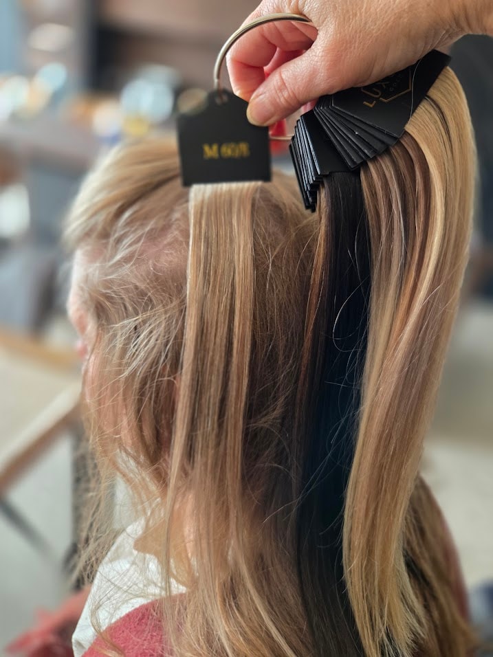 Hand met een waaier van clip-in extensions in verschillende tinten die worden afgestemd op natuurlijk haar