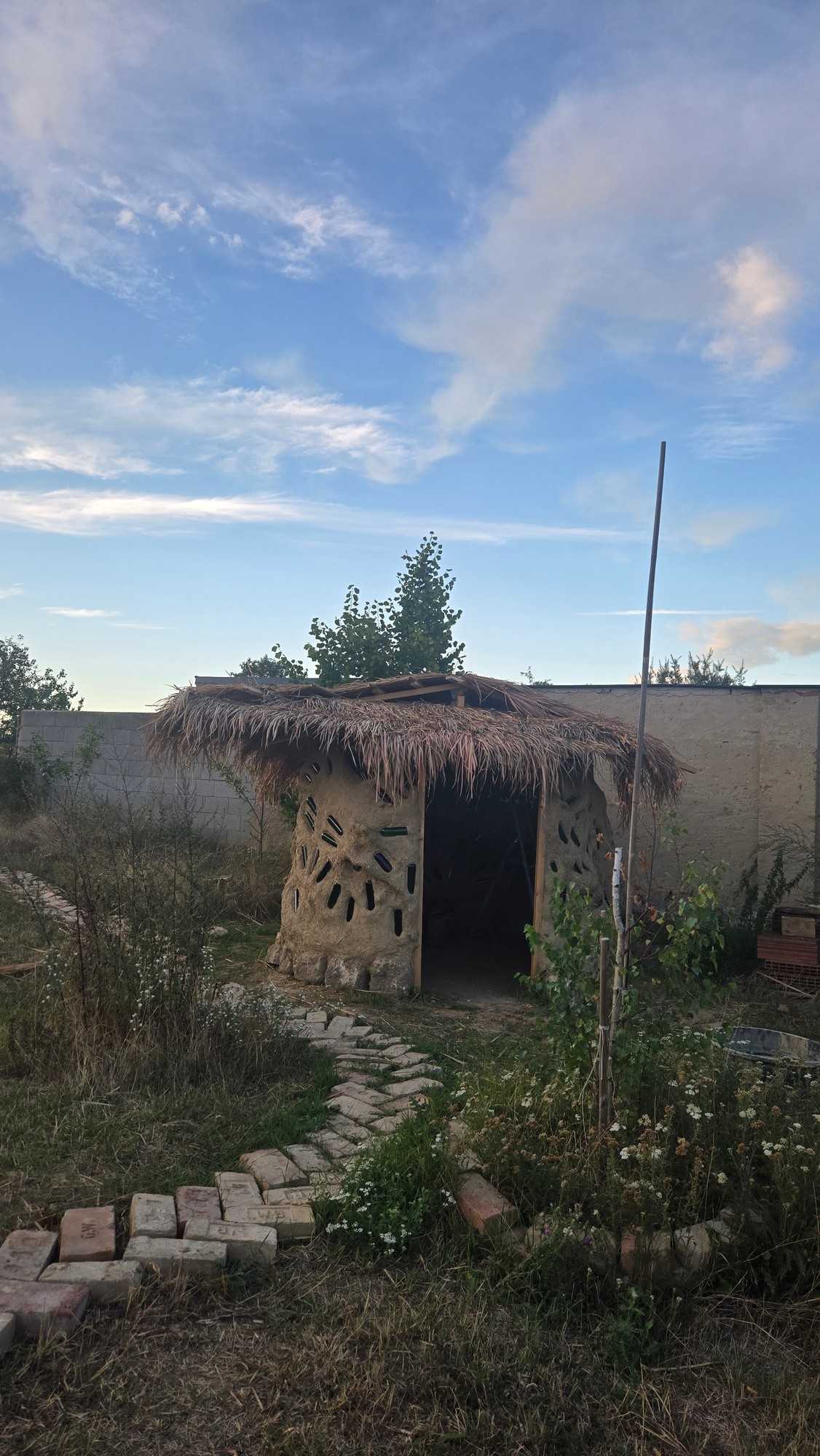 Außenansicht der selbst gebauten Lehmhütte mit Reetdach im Abendlicht