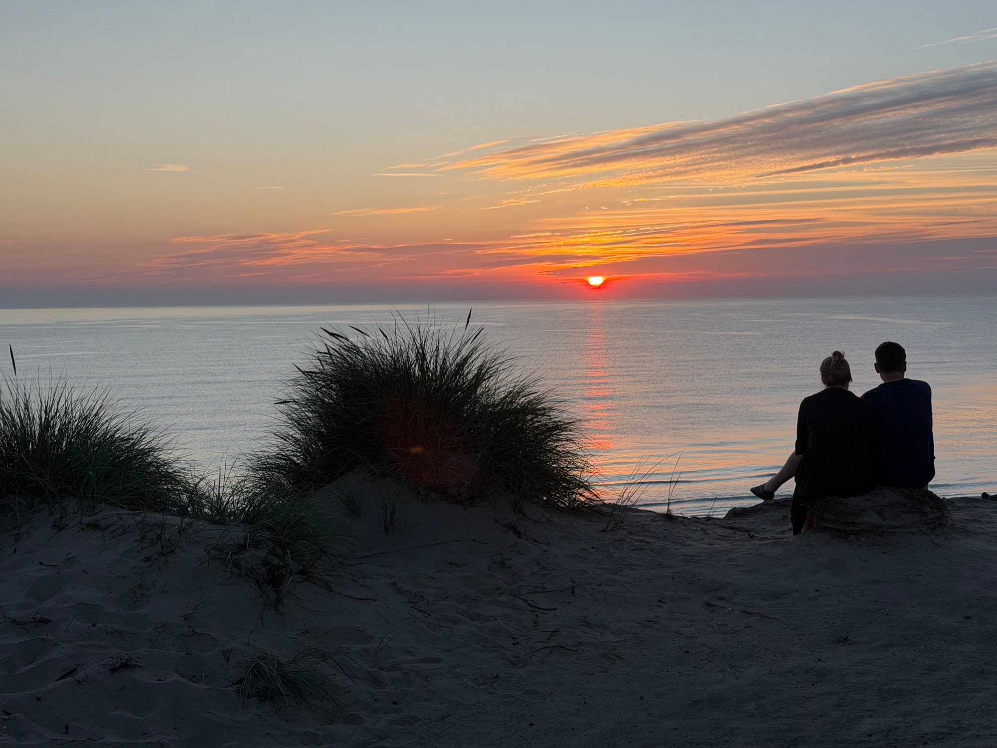 Par sidder hånd i hånd og ser mod solnedgangen over havet