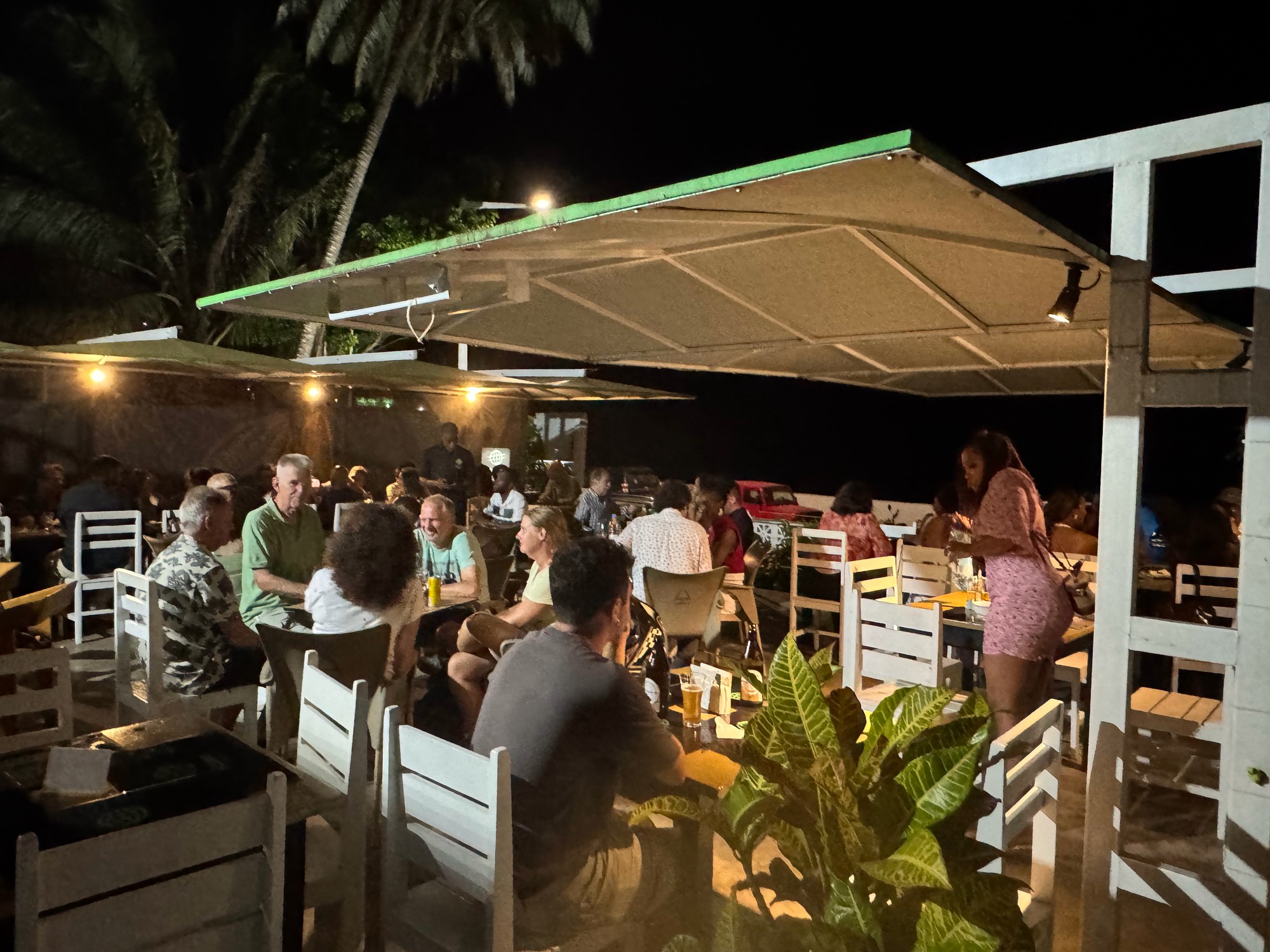 Busy terrace at Kalipso bar in São Tomé at night, diners seated under large umbrellas beside the sea