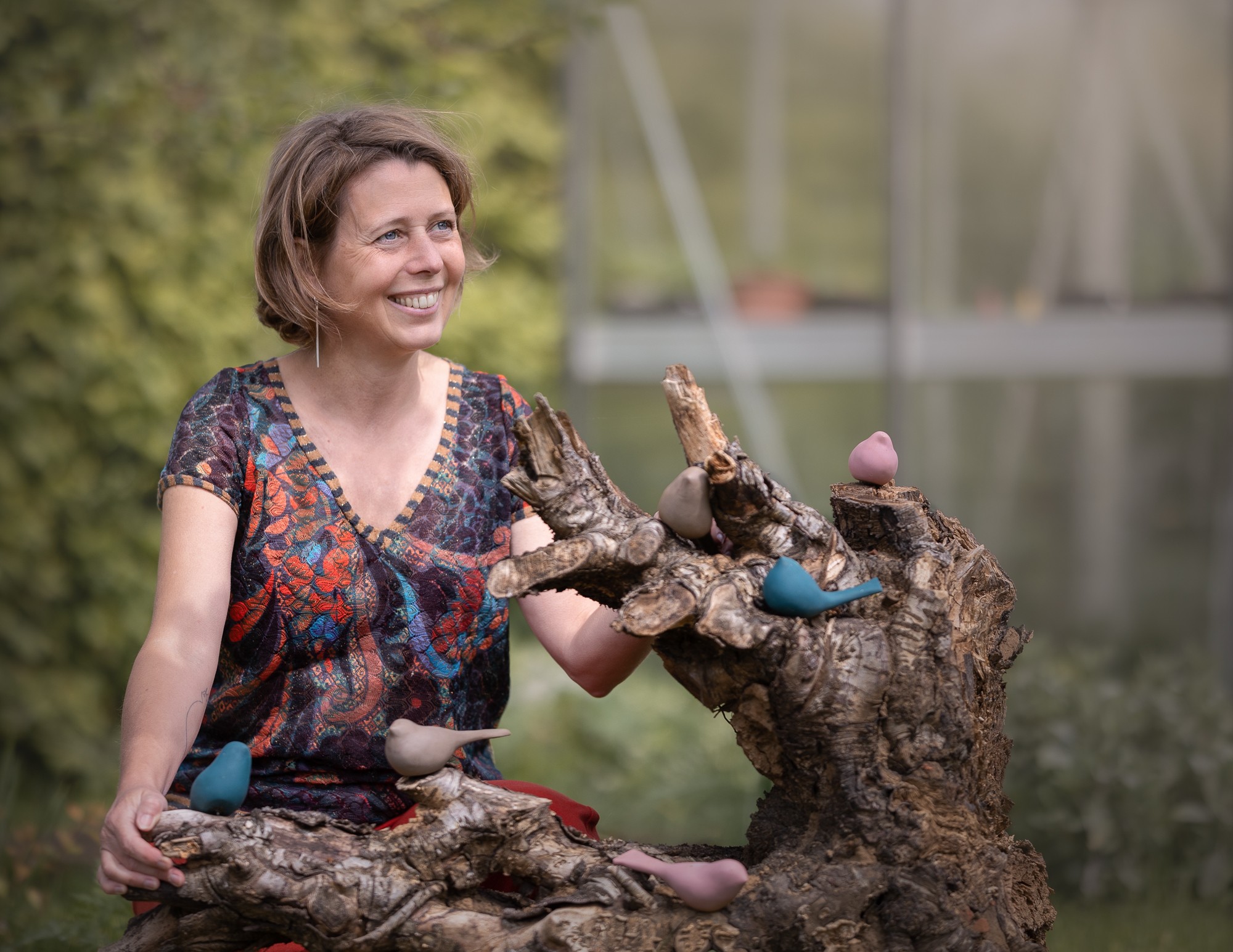 Nathalie Hendrickx met haar porseleinen vogels op een boomstronk in de tuin