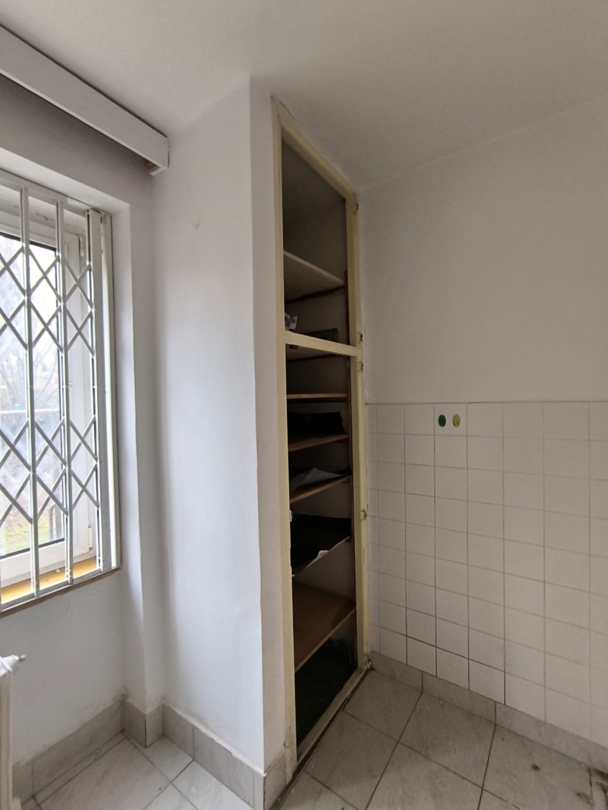 Původní kuchyň s vestavěným regálem a bílým obkladem.