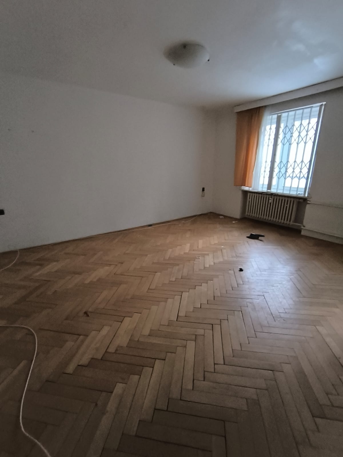 Obývací pokoj v původním stavu — parkety, starší radiátor.