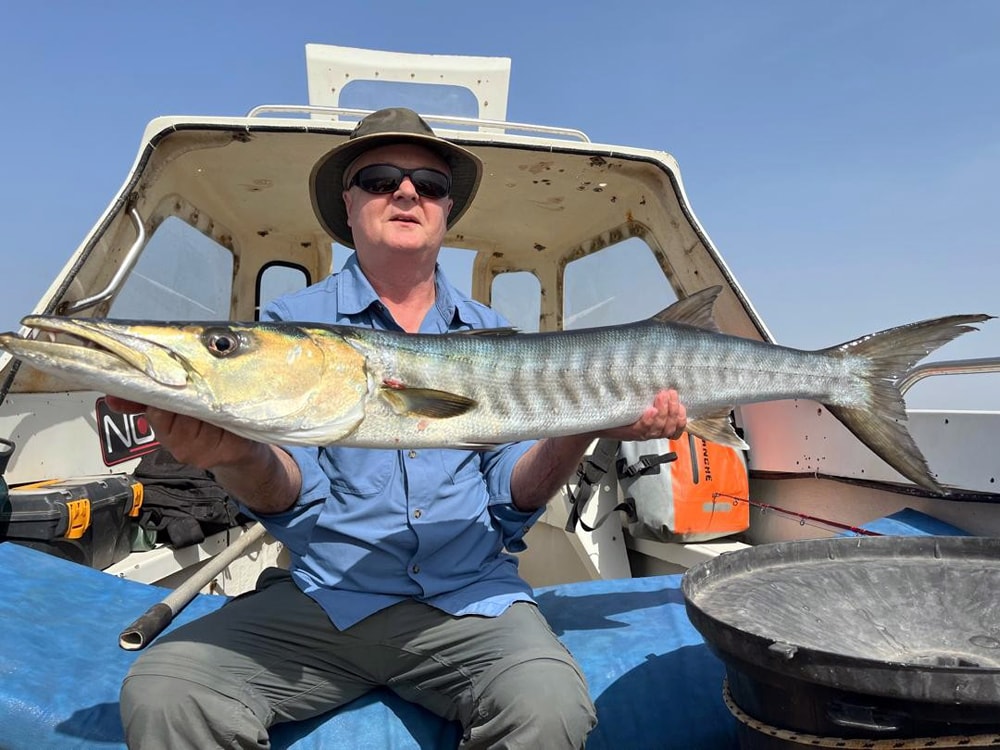 Glad lystfisker med en kraftig trevally i gyldent lys