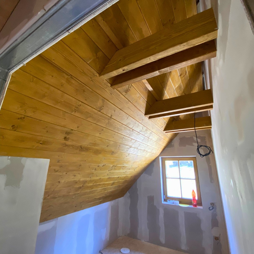 Interiér podkroví — dřevěný podhled s přiznanými trámy a SDK sádrokartonové stěny připravené k omítání