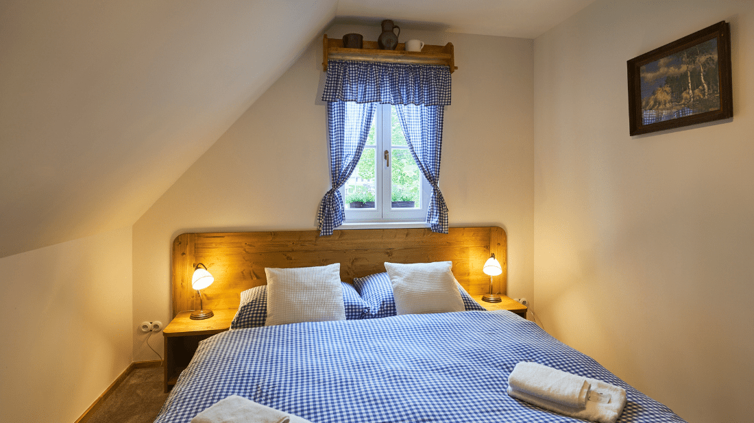 Ložnice v podkroví s dřevěným čelem postele a venkovskými závěsy