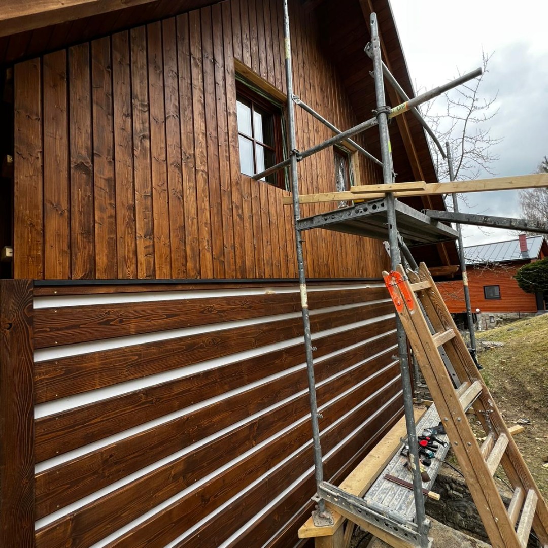 Detail pokládky falešného roubení — horizontální KVH profily na fasádě chaty během montáže na lešení