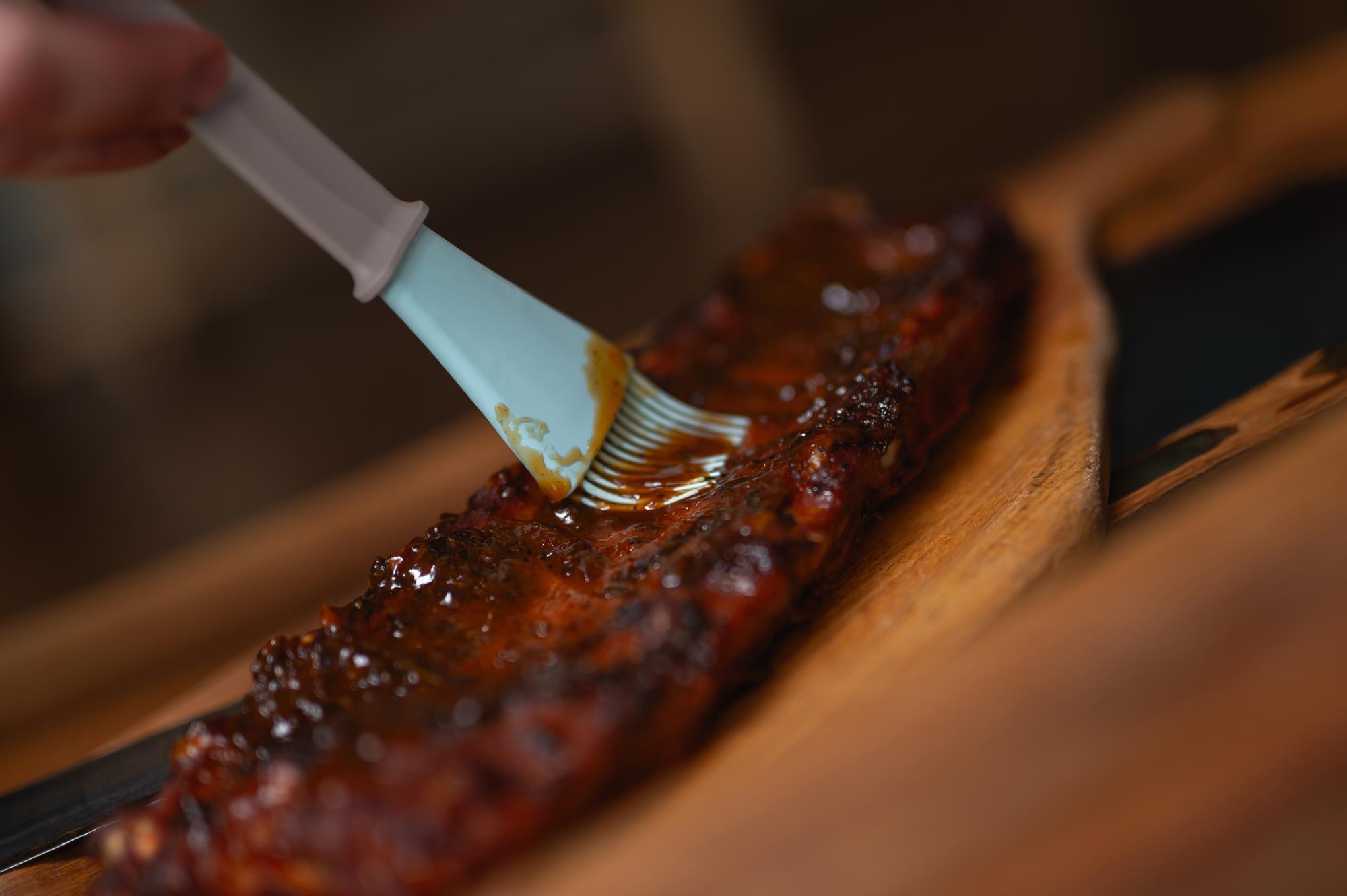 BBQ kefa nanáša medovú marinádu na rebrá — detailný záber glazovania