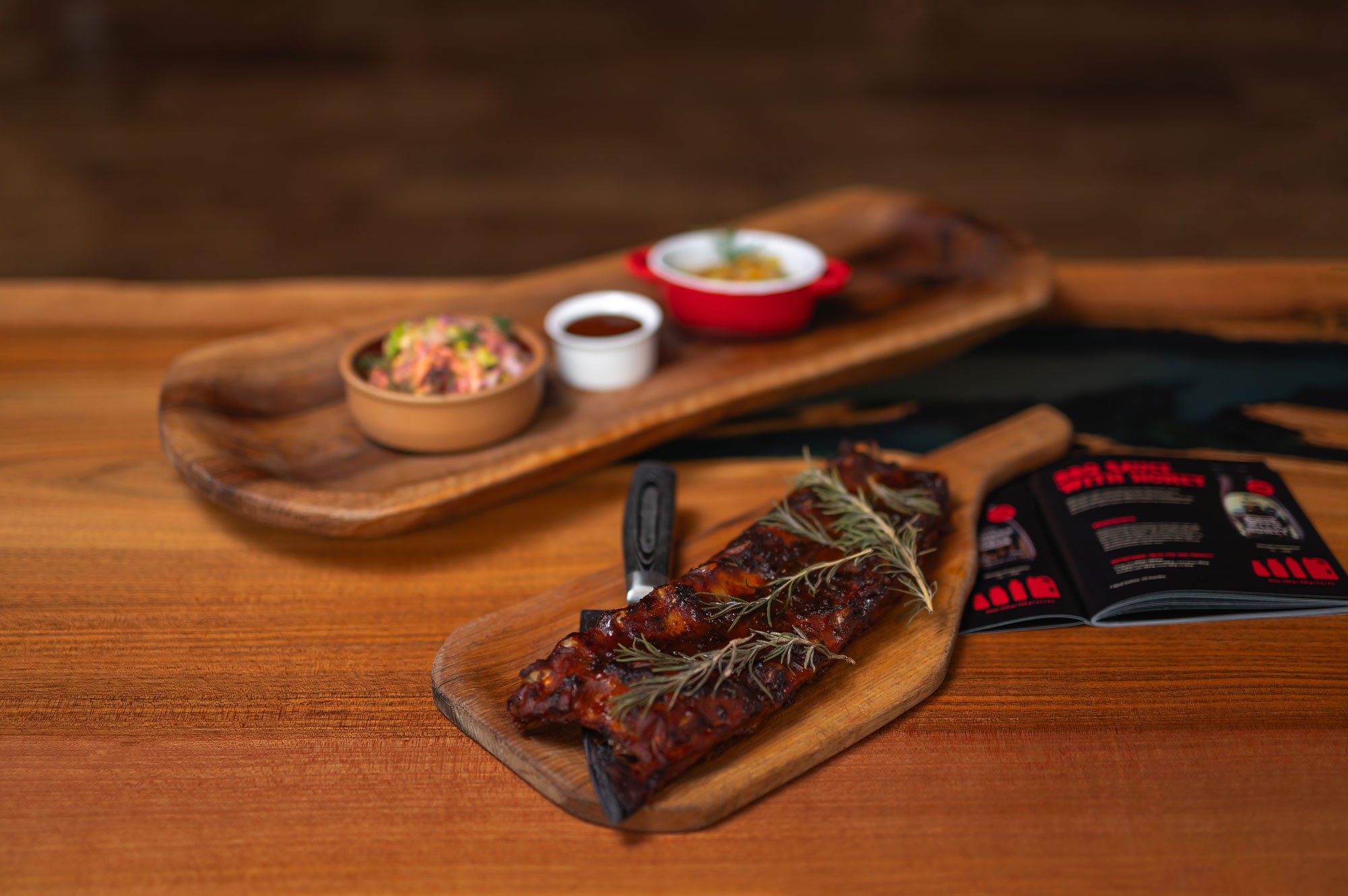 Celý bok rebier na servírovacom prkne s OAK & BBQ brožúrou — atmosferický záber