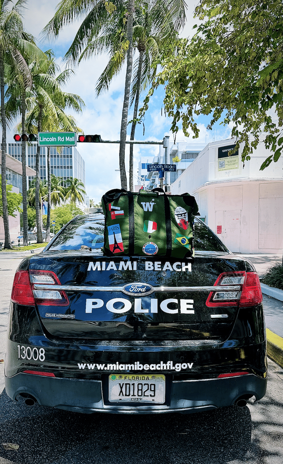 A green WISSHH Travel Bag with travel stickers on the trunk of a Miami Beach Police patrol car