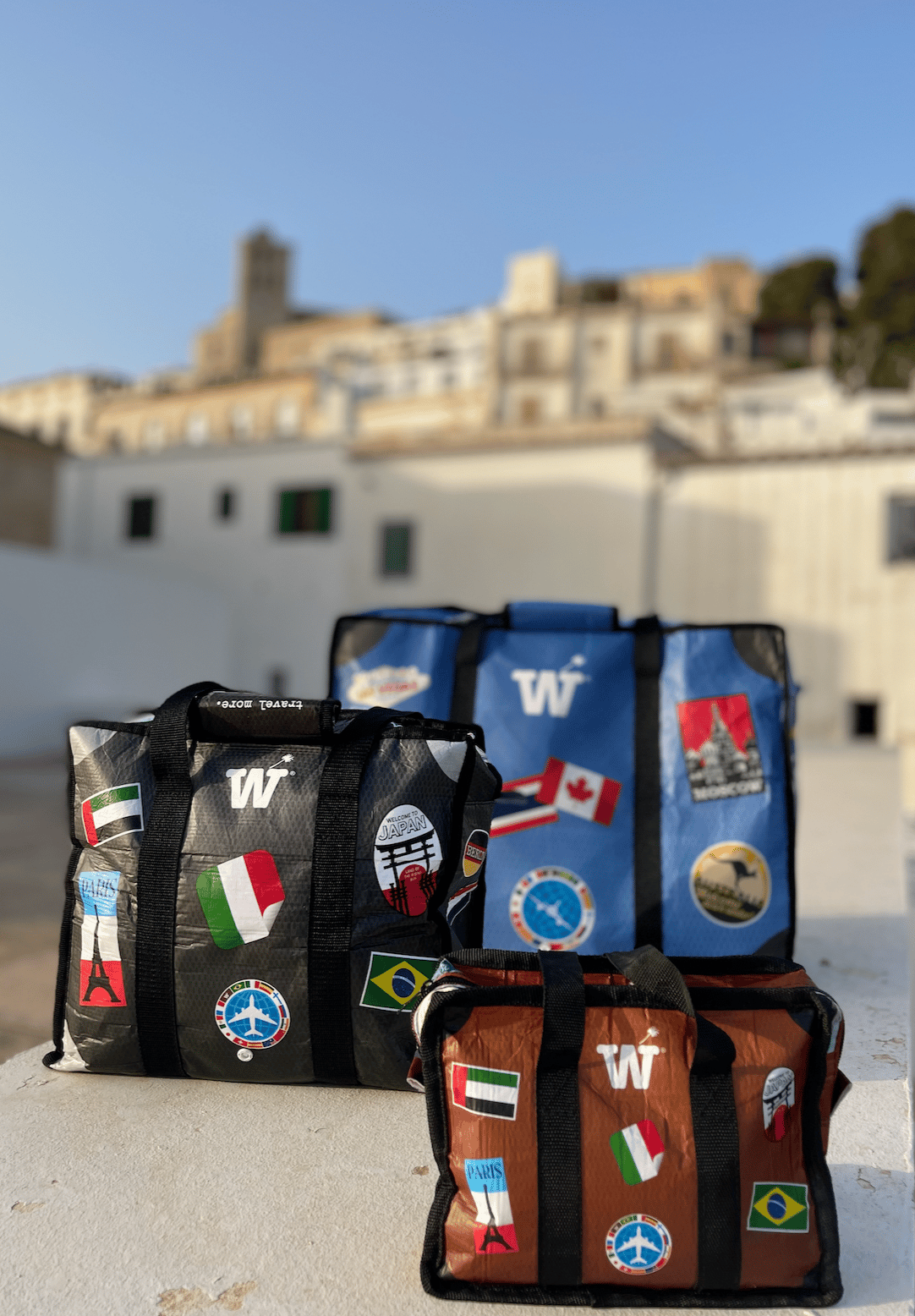 Black, blue and brown stickered WISSHH Travel Bags in a whitewashed Mediterranean old town