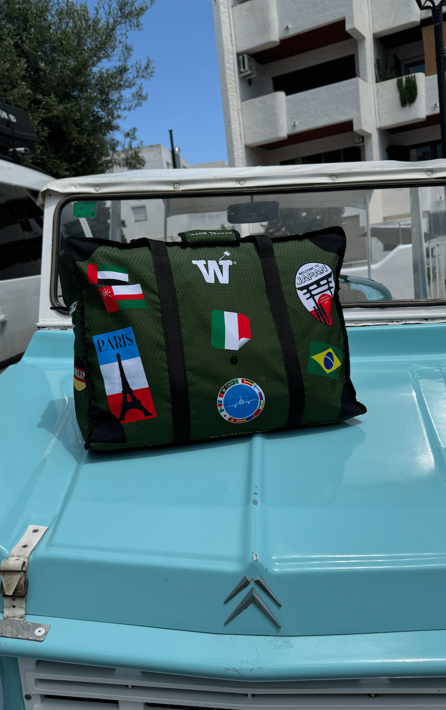 A green WISSHH Travel Bag with travel stickers on the hood of a turquoise vintage Citroën Méhari