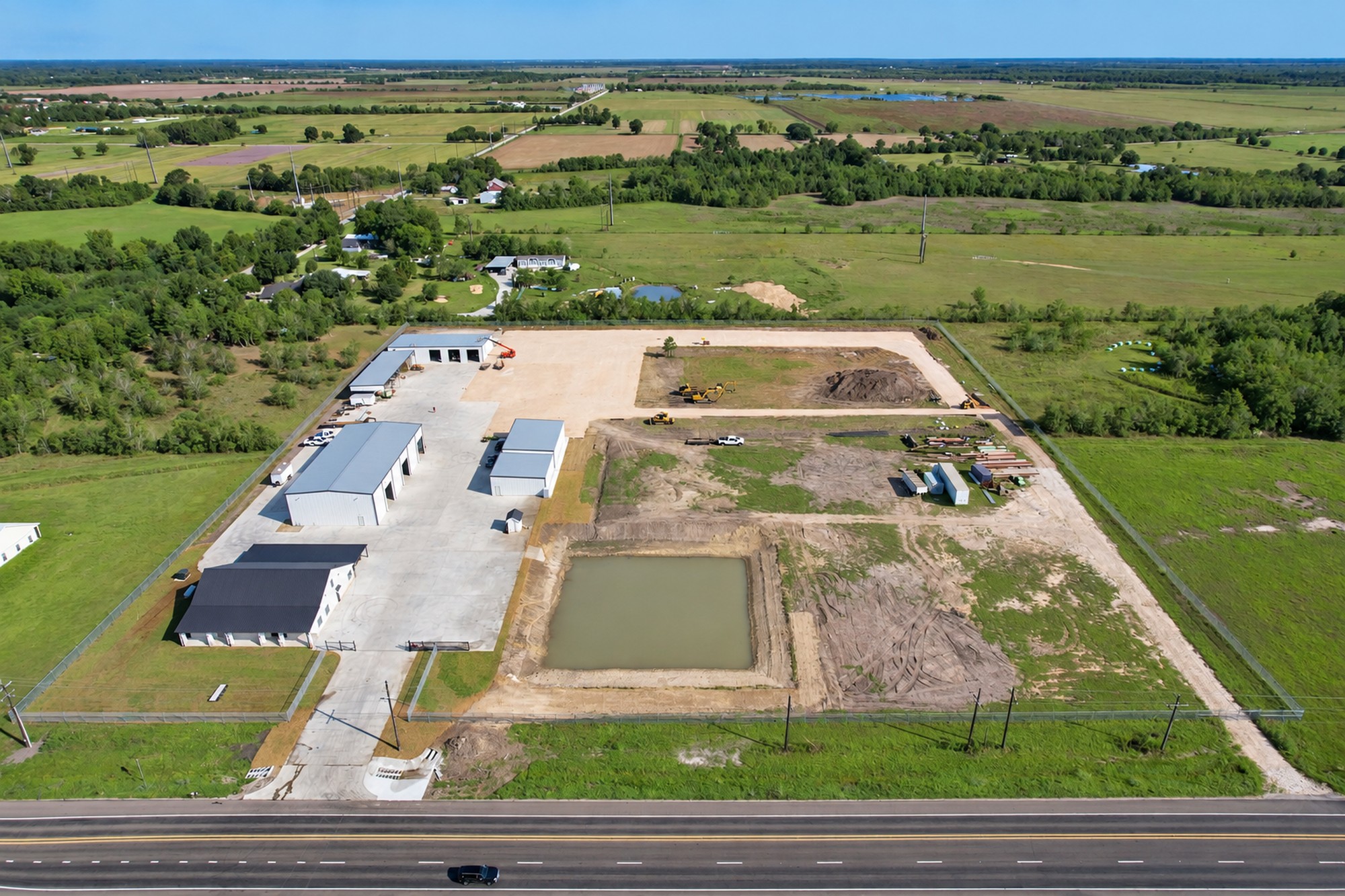 Aerial drone photo of a Houston-area commercial property with warehouses, equipment yard, and detention pond