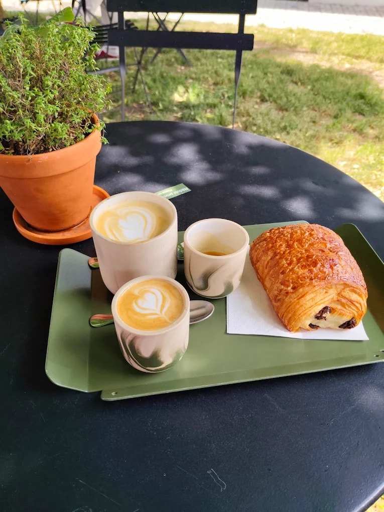 Dvě latté a croissant na zeleném tácu venku