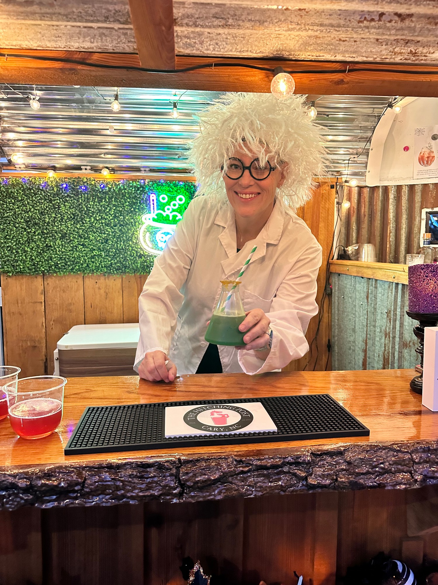 Lisa in mad scientist costume holding a green beaker cocktail at The Hitching Post bar
