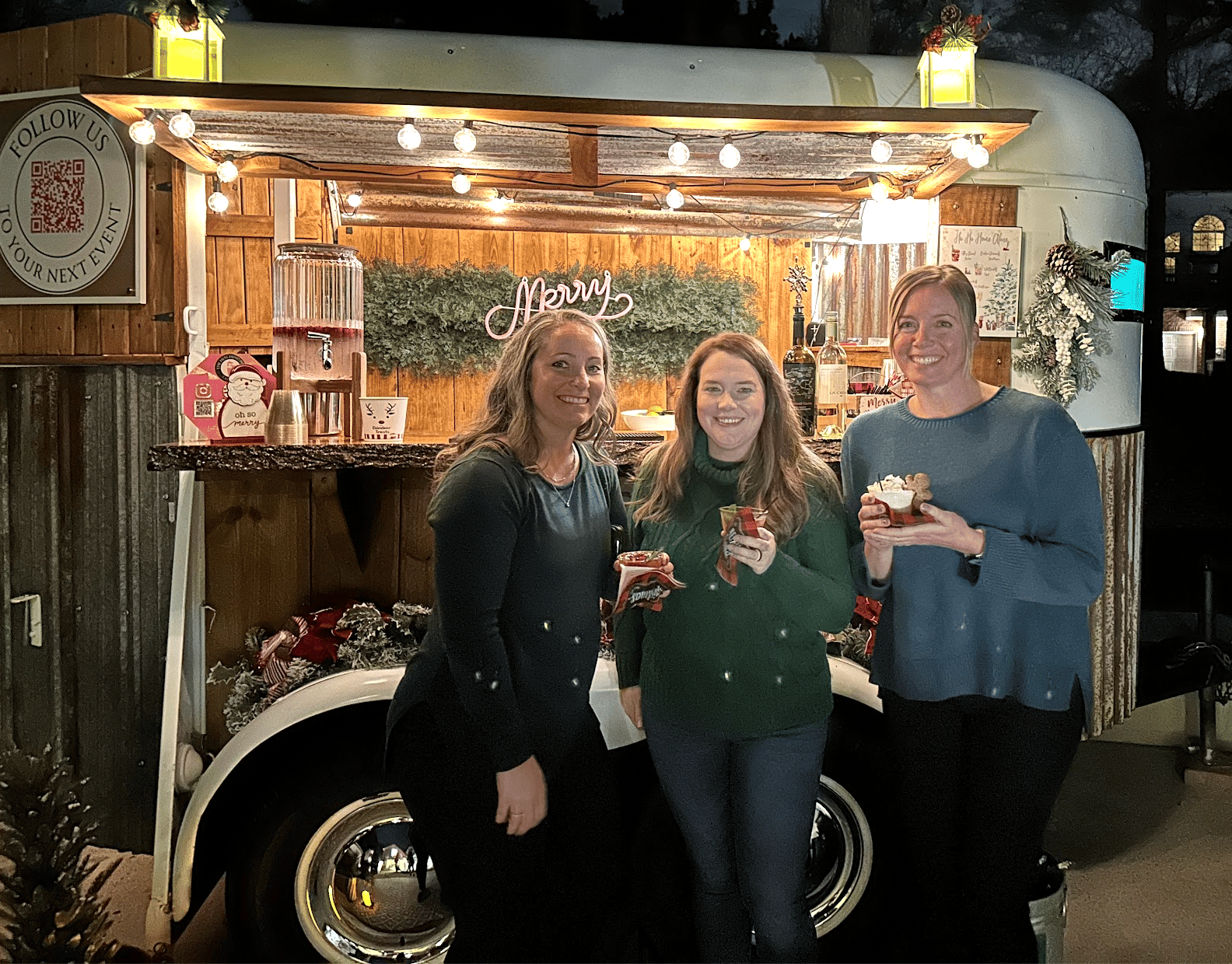 Guests smiling with holiday cocktails in front of The Hitching Post trailer decorated for a corporate holiday party