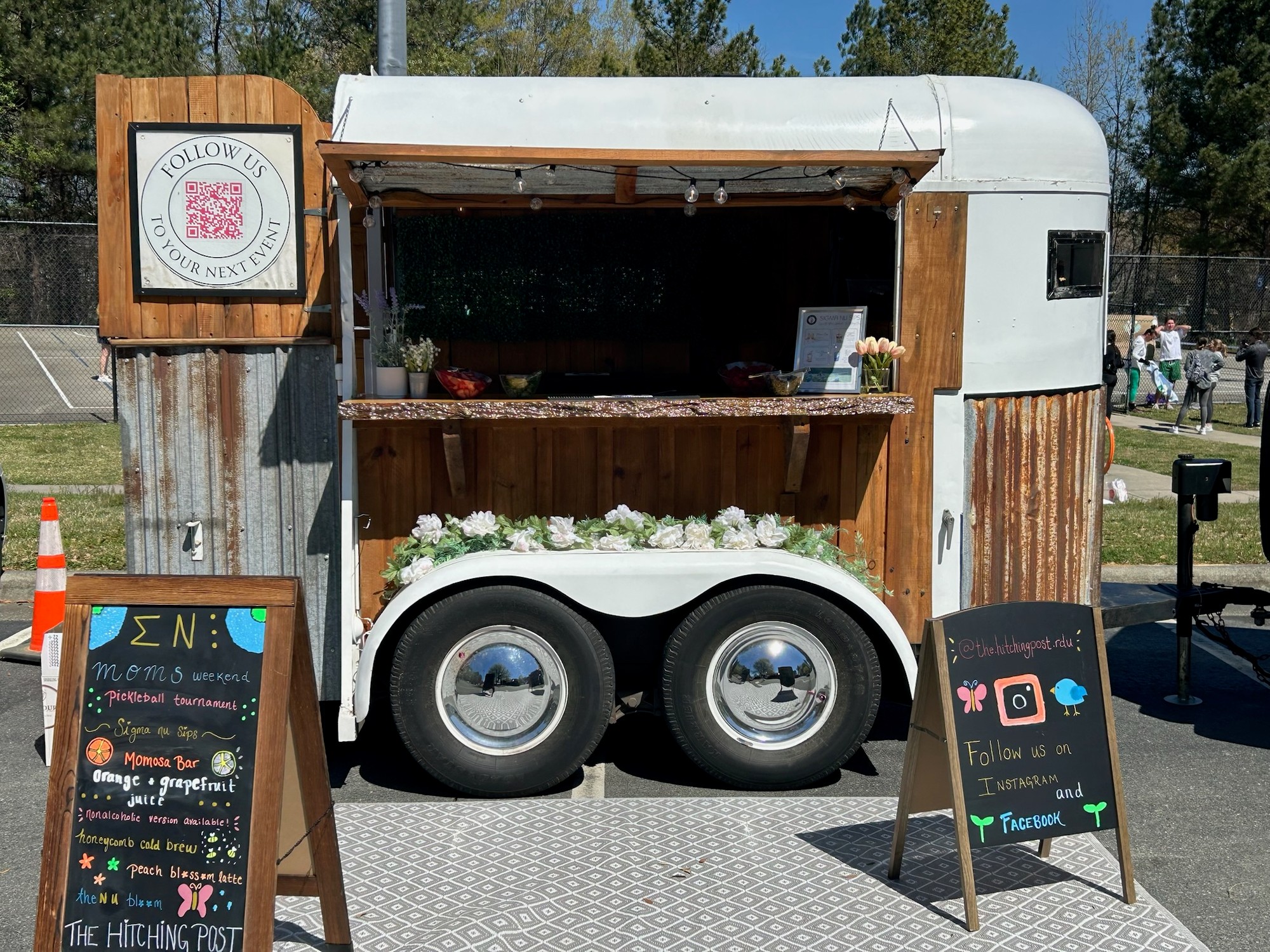 The Hitching Post trailer set up for Sigma Nu Moms Weekend with Momosa Bar, Honeycomb Cold Brew, and Peach Blossom Latte on the chalkboard