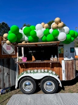 The Hitching Post trailer decorated with green, white, and gold balloon garland for Omega Phi Alpha NAMI philanthropy event