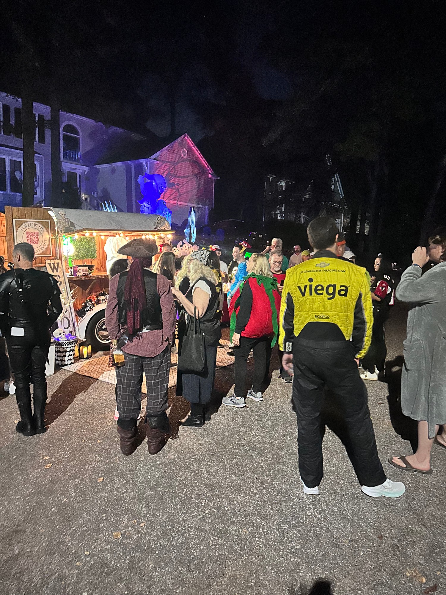 Crowd of costumed guests gathered around The Hitching Post trailer at night during a Halloween neighborhood event