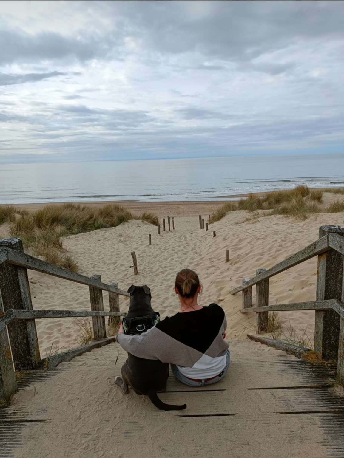 An en haar hond Shiva samen op de duintrap uitkijkend over zee