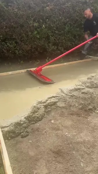 Worker leveling concrete mix across the slab with a bull float