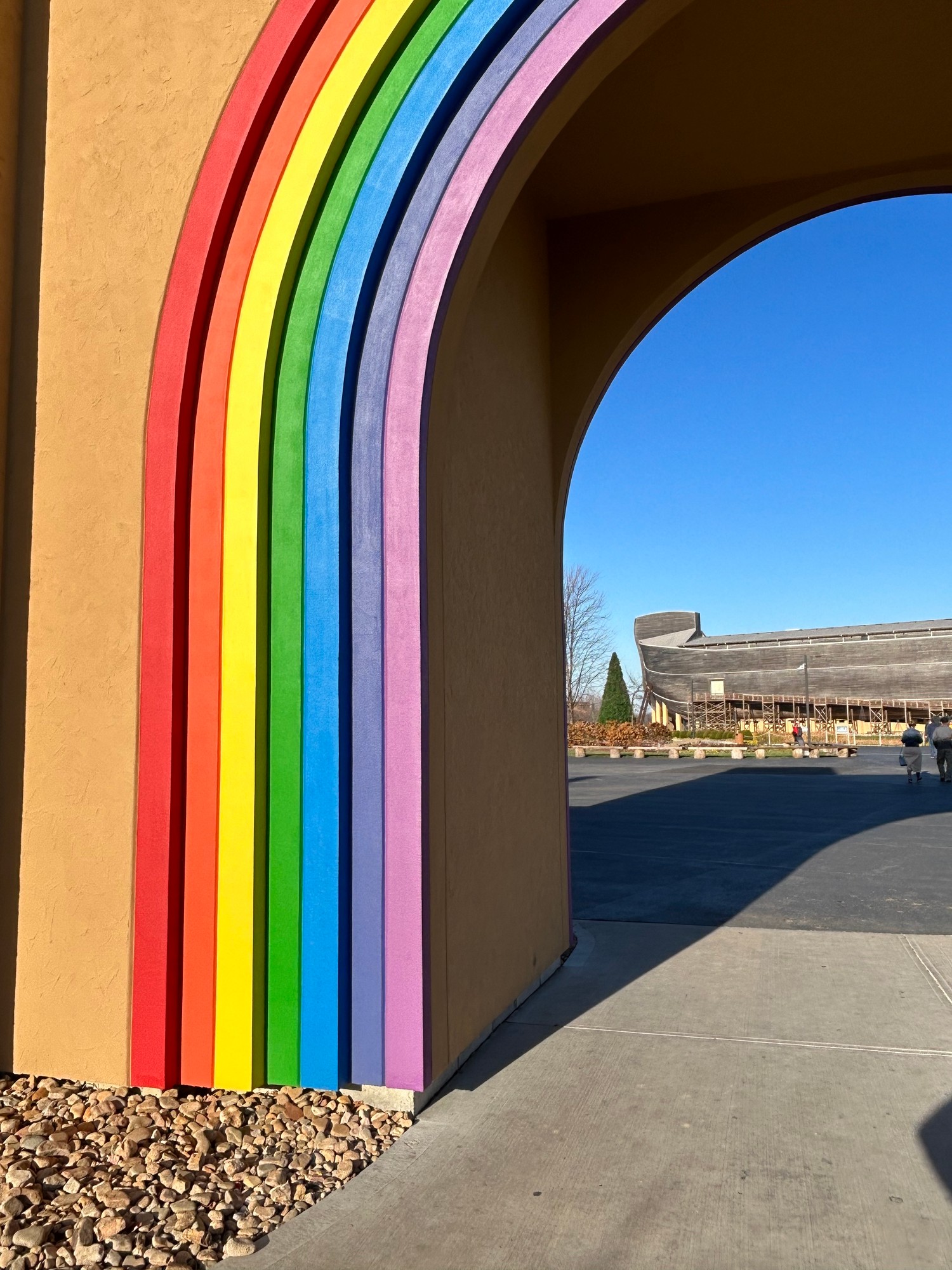 A rainbow-painted archway at the Ark Encounter, with the Ark itself in the background