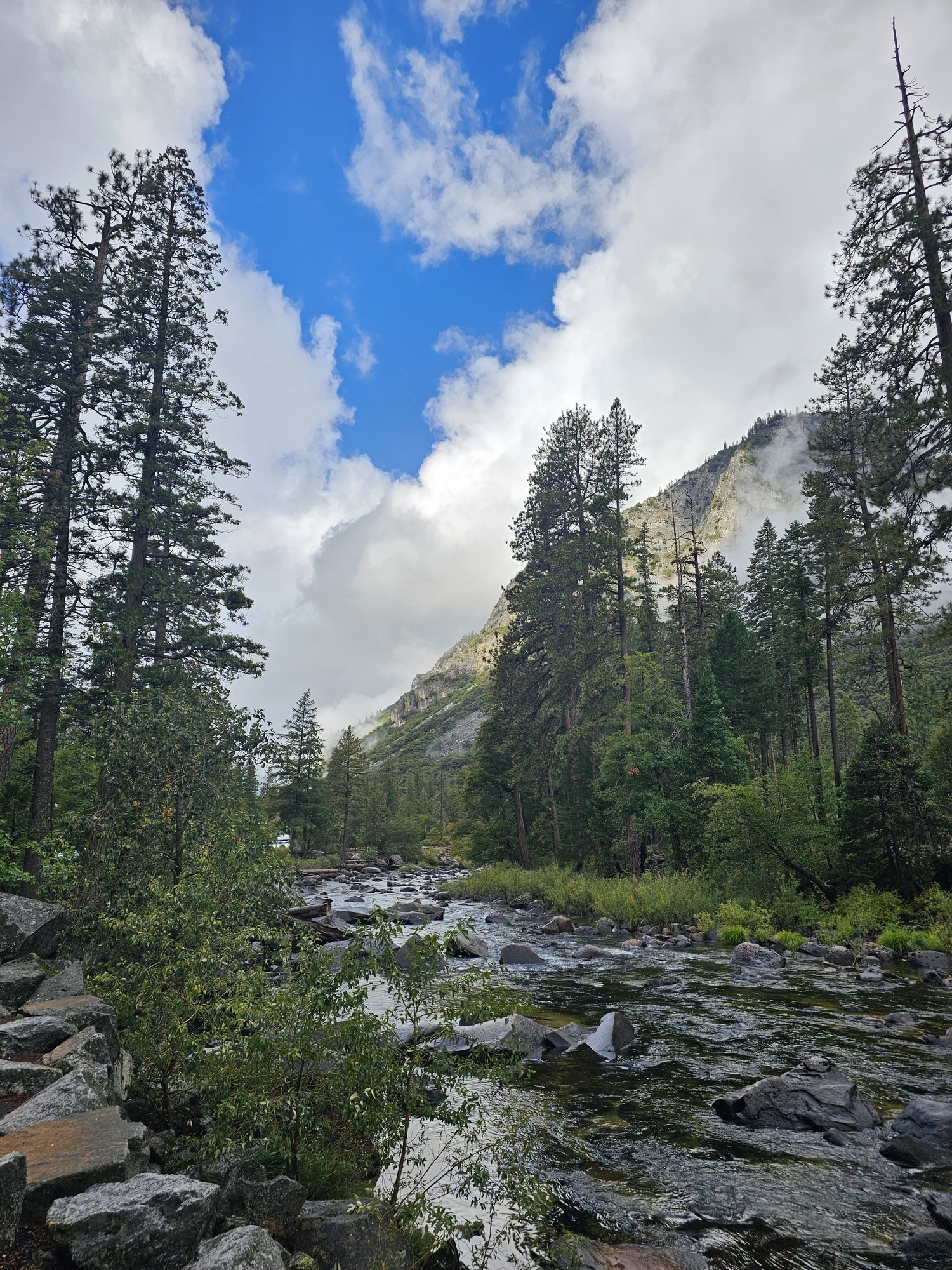 The Merced River running over rocks through Yosemite Valley, with granite peaks behind