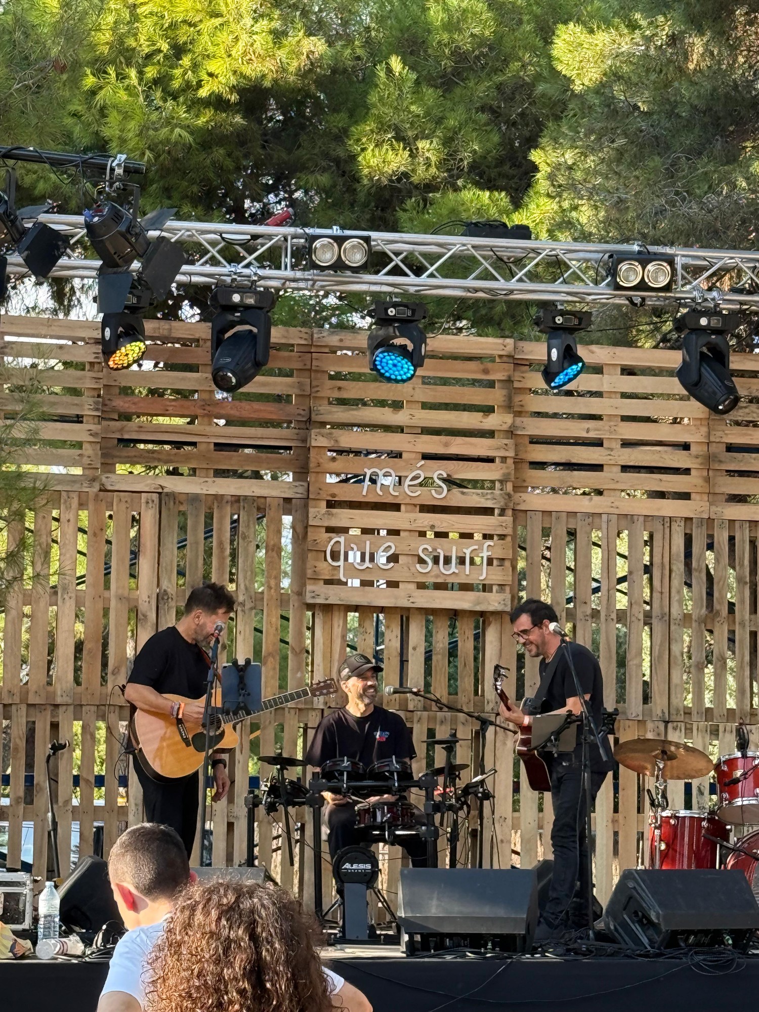 Joan Tena y dos músicos tocando en directo en un escenario exterior de madera durante una celebración privada