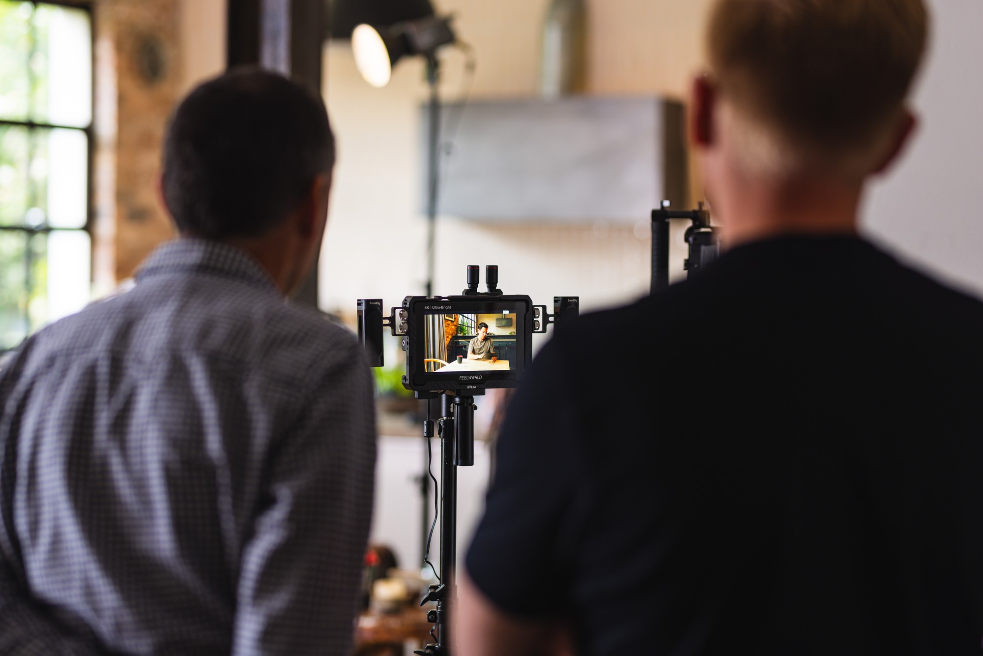 A producer keeps watch at the monitor during a filmed interview in a red-toned venue